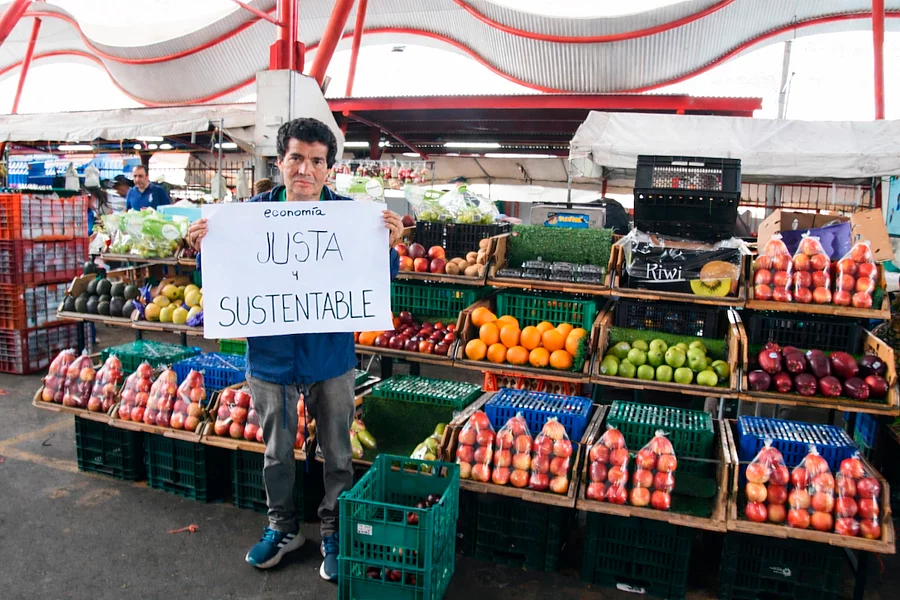 Hombre en feria del agricultor sosteniendo cartel sobre economía justa y sustentable.